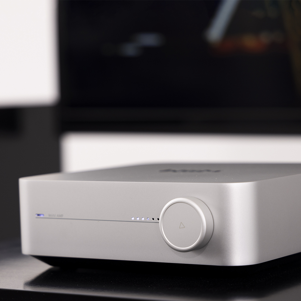 WiiM Amp and Arcam Radia A5 side by side with speakers on a shelf