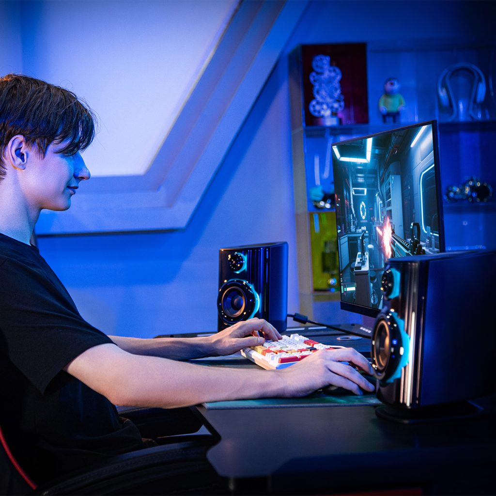a teeenager playing videogames on his computer in a mordern room with the oxs thunder duo speakers on show